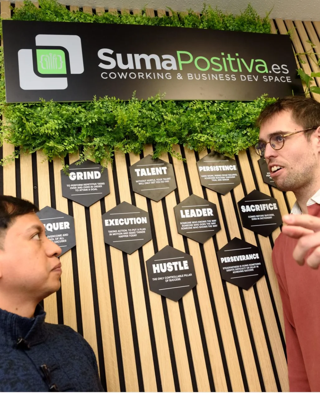 Pared de valores de SumaPositiva.es con hexágonos, y dos personas conversando